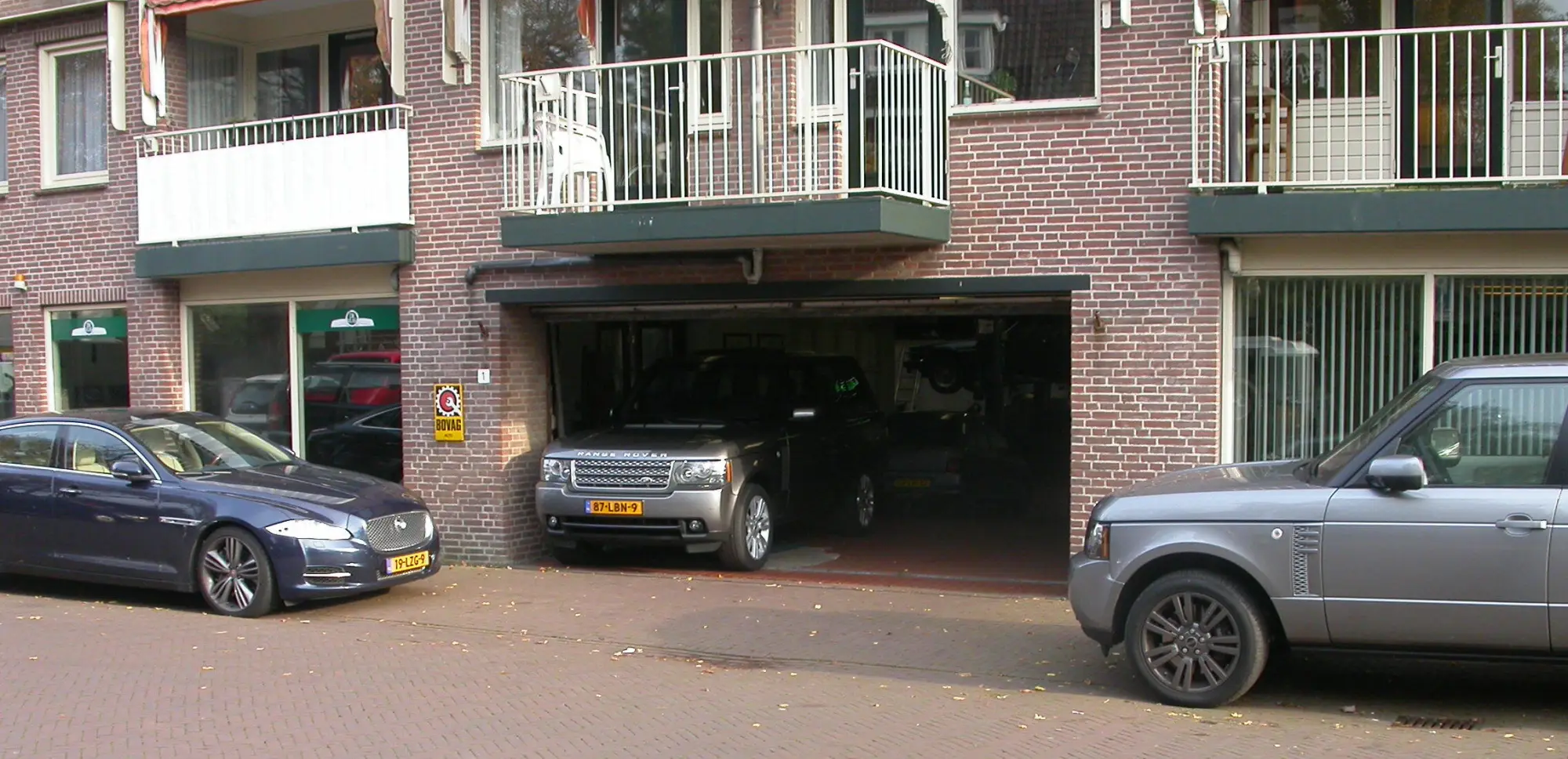De geopende garagedeur van De Vlas aan de Bloemendaalseweg 1, met een Range Rover in de deuropening en een Jaguar voor de deur