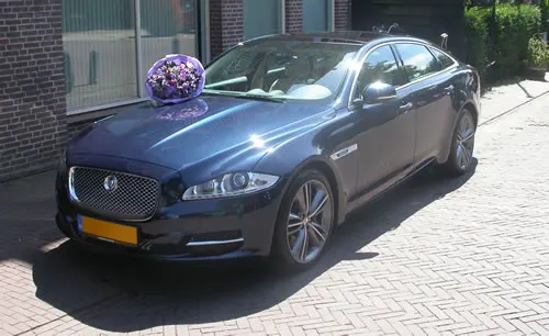 Een donkerblauwe Jaguar XJ met een bloemstuk op de motorkap voor de garage