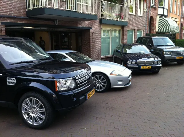 Een Land Rover Discovery, een Jaguar XK, een Jaguar XJ en een Range Rover voor de geopende garagedeur van De Vlas